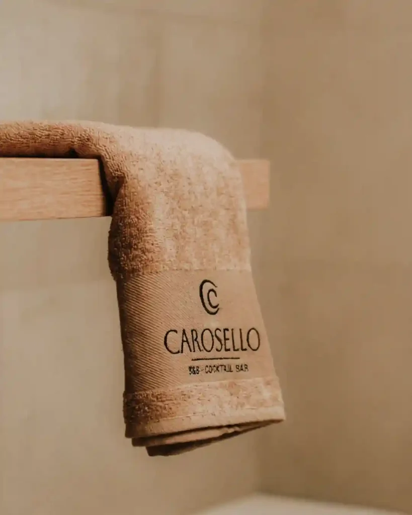 Set di biancheria personalizzata al B&B Carosello: dettaglio di asciugamano bianco con logo ricamato all'Isola d'Elba."