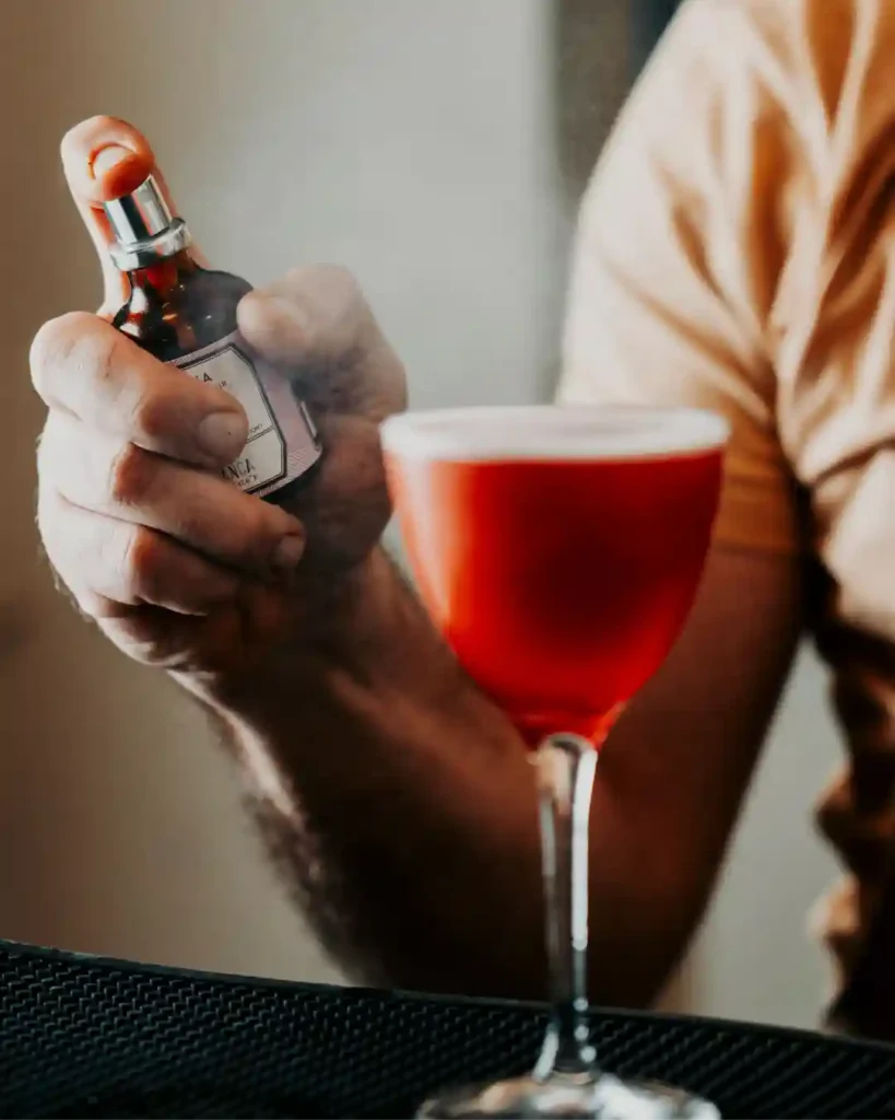 Preparazione cocktail artigianale al B&B Carosello: dettaglio di un aroma spruzzato su un drink rosso per gli ospiti all'Isola d'Elba.